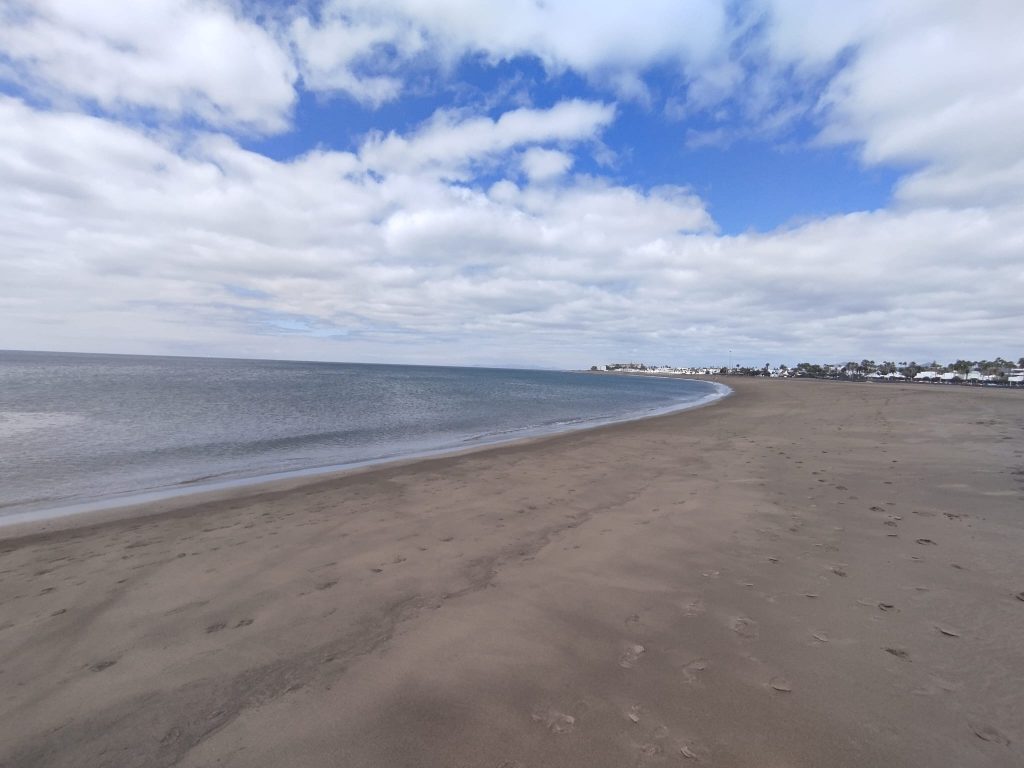 Strand rechts, links Meer, Himmel mit hellen Wolken