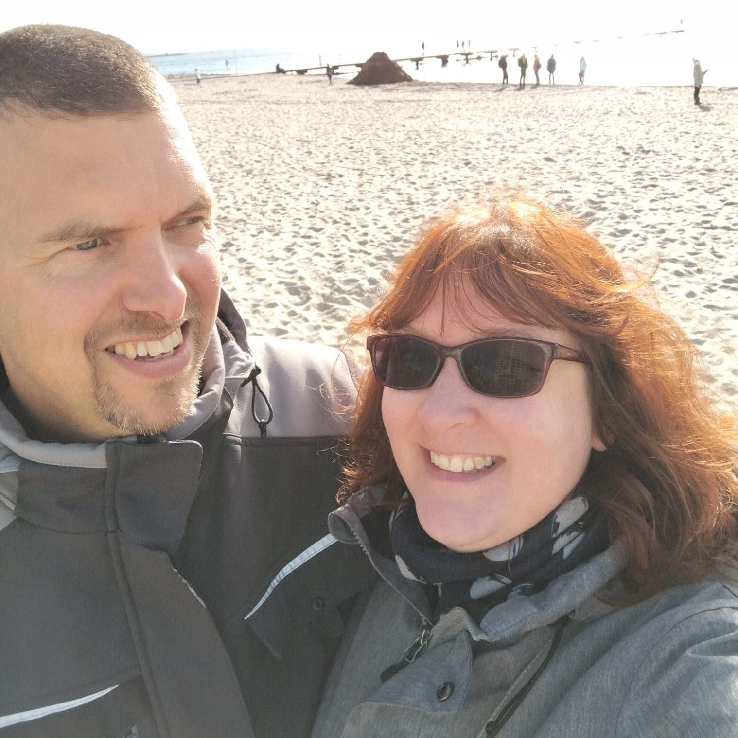 Mann und Frau lachen in die Kamera dahinter Strand